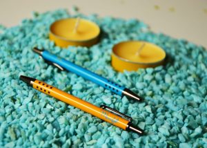 Bolígrafos mini metálicos varios colores junto a dos velas
