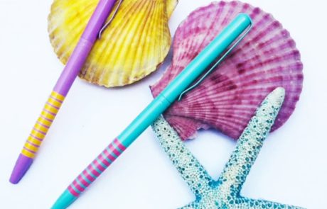 Bolígrafos estrechos rayas varios colores sobre conchas marinas