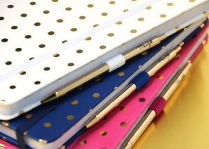 Cuadernos puntos con bolígrafos varios colores apilados